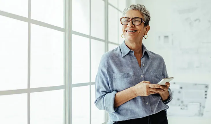A, older, female facilities user smiles up from her phone in a brightly lit, mostly white office environment.
