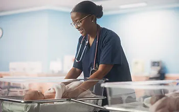 A doctor visits a maternity ward to check on an infant, both are smiling at each other and the dr wears a stethescope around her neck.