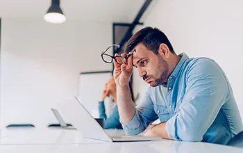 A facilities manager exhales, looking stresseed, while looking at a laptop screen