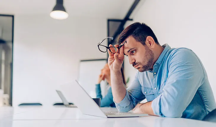A facilities manager exhales, looking stresseed, while looking at a laptop screen