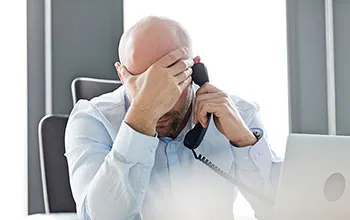 A facilities manager drops his head into his hand in frustration while talking on a landline phone