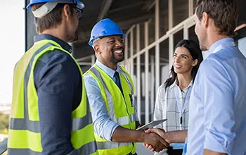 A contractor in a safety vest and hard hat shakes hands with a facility manager