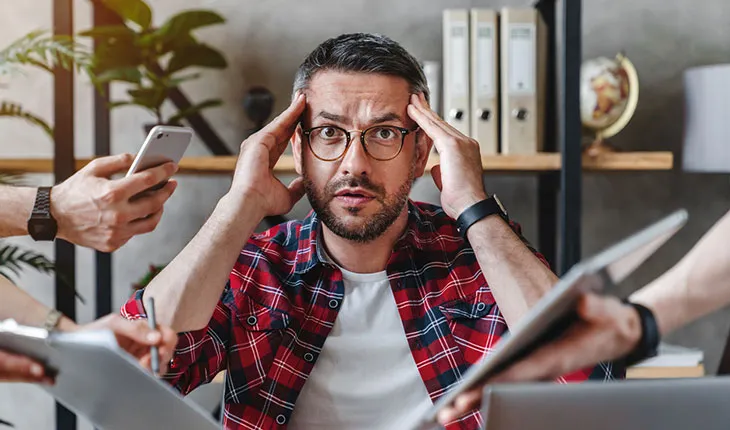 A facilities manager appears overwhelmed as multtiple hands holding phones, contracts and papers compete for attention