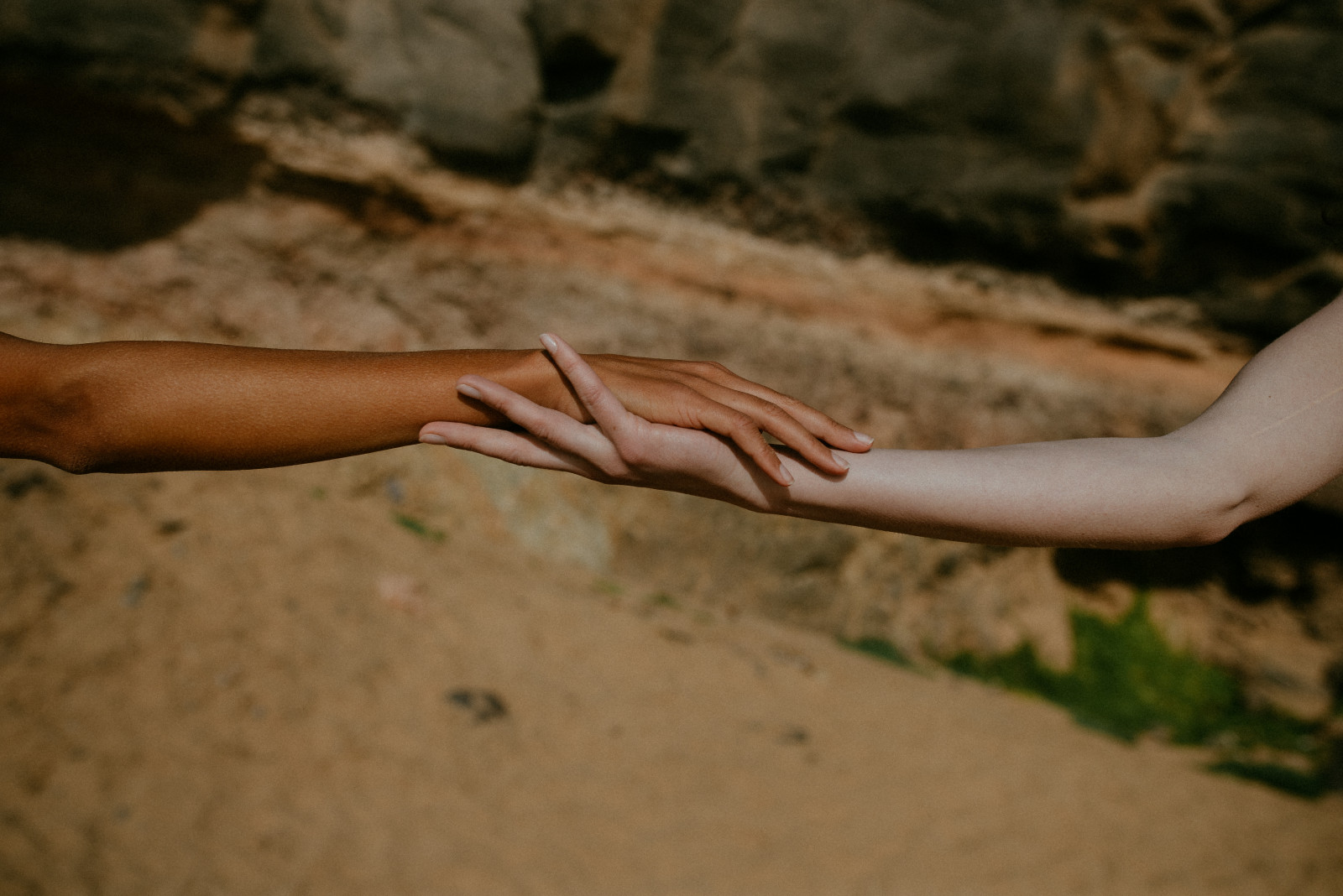 Two hands holding against a backdrop of sand and rocks.
