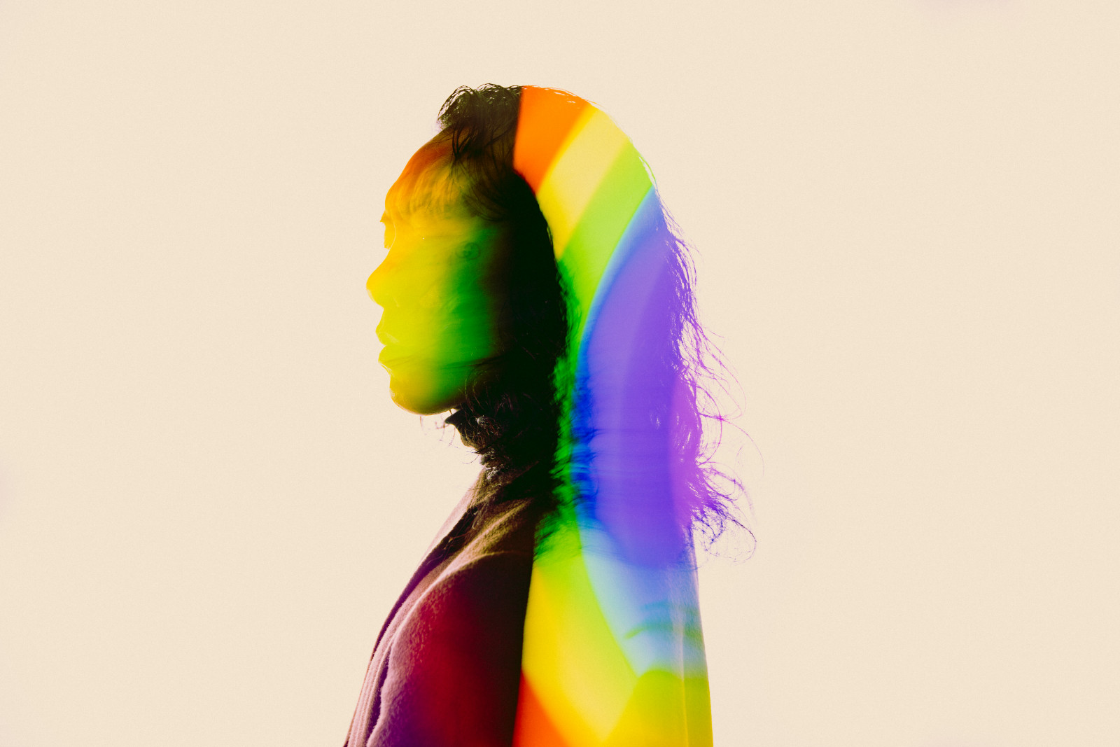 A rainbow-lit silhouette of a person in profile, against a cream background.