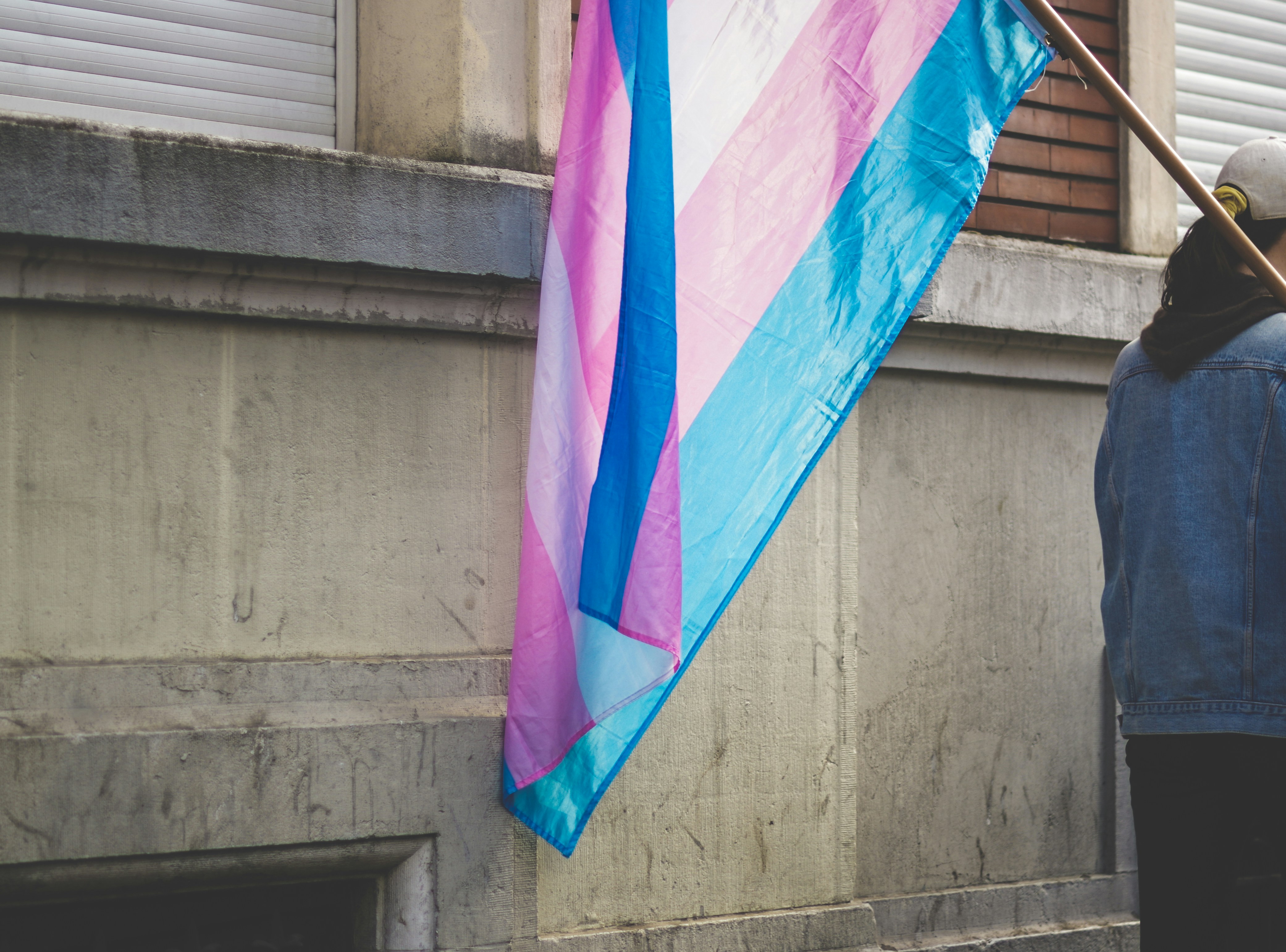 A person walking away with a trans flag balanced over their shoulder.