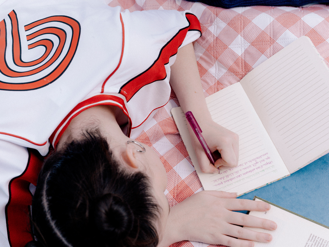 A shot from above of the back of a person's head as they write in a journal.