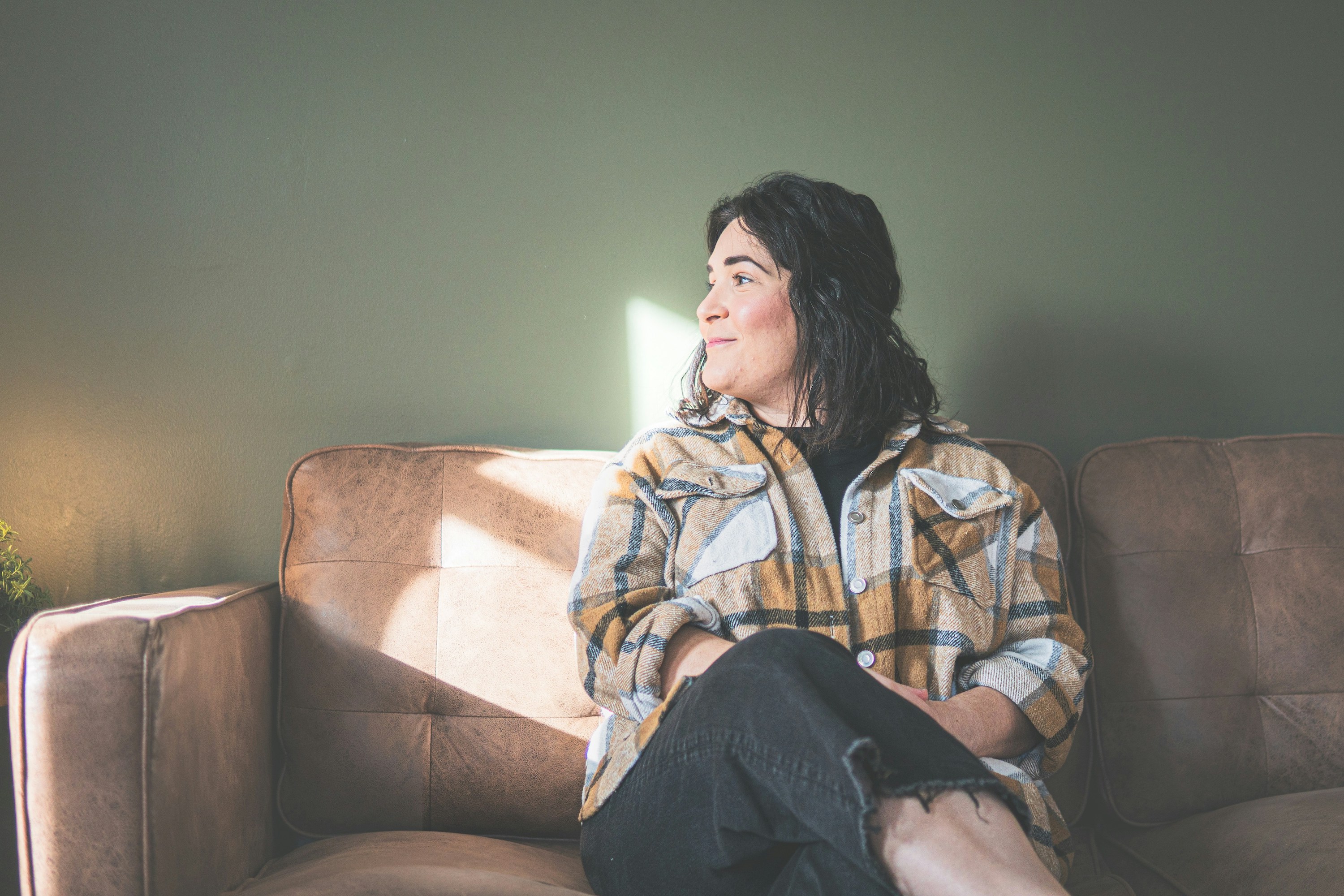 A woman sitting on a sofa looking in the direction of sunlight.