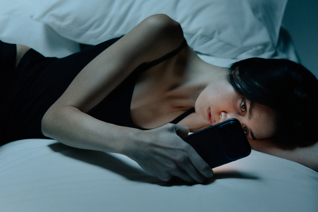 A white woman stares at the blue light of her phone in bed.