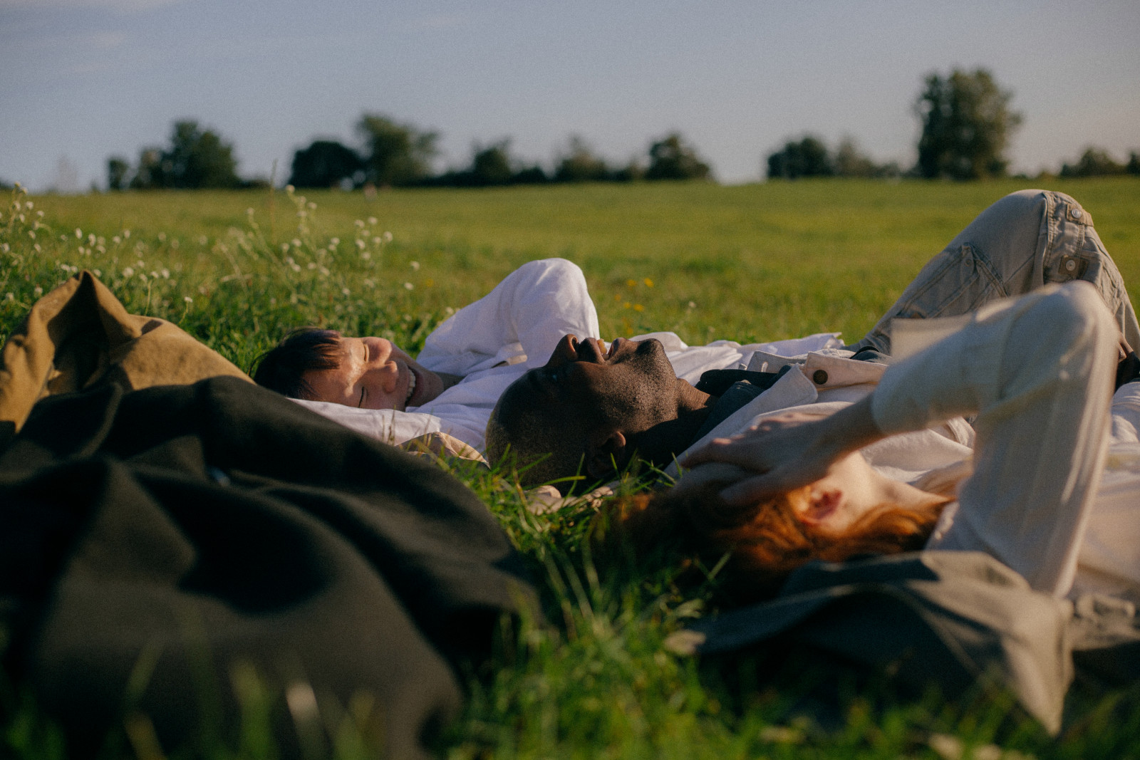 Three people lying back and laughing in a field. 