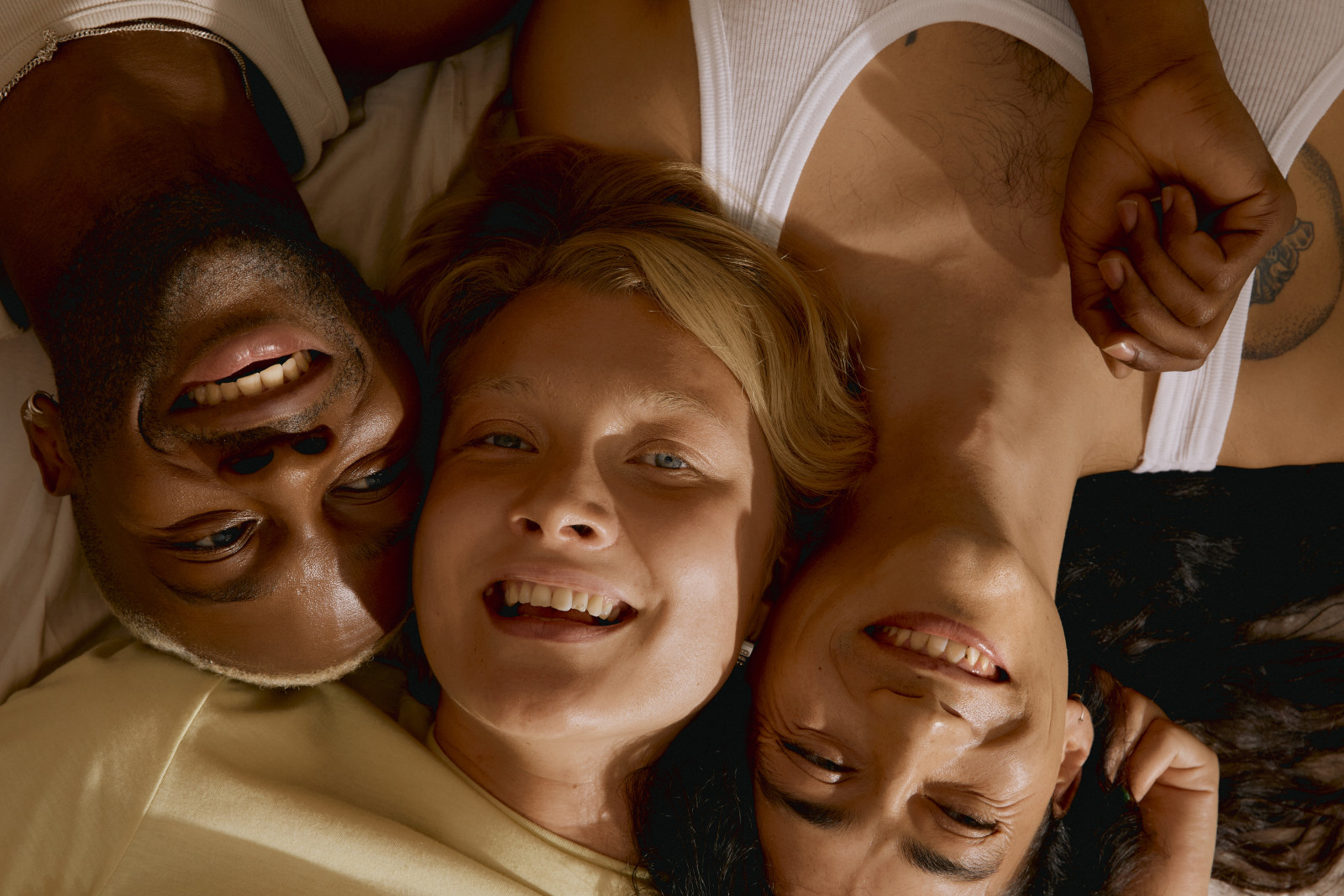 Three friends lying on their backs smiling up at the camera.