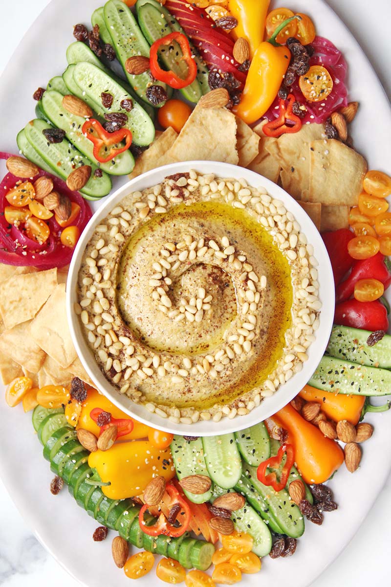 Beautiful mezze platter with eggplant hummus in the middle, surrounded by pita chips, vegetables, and fruits.