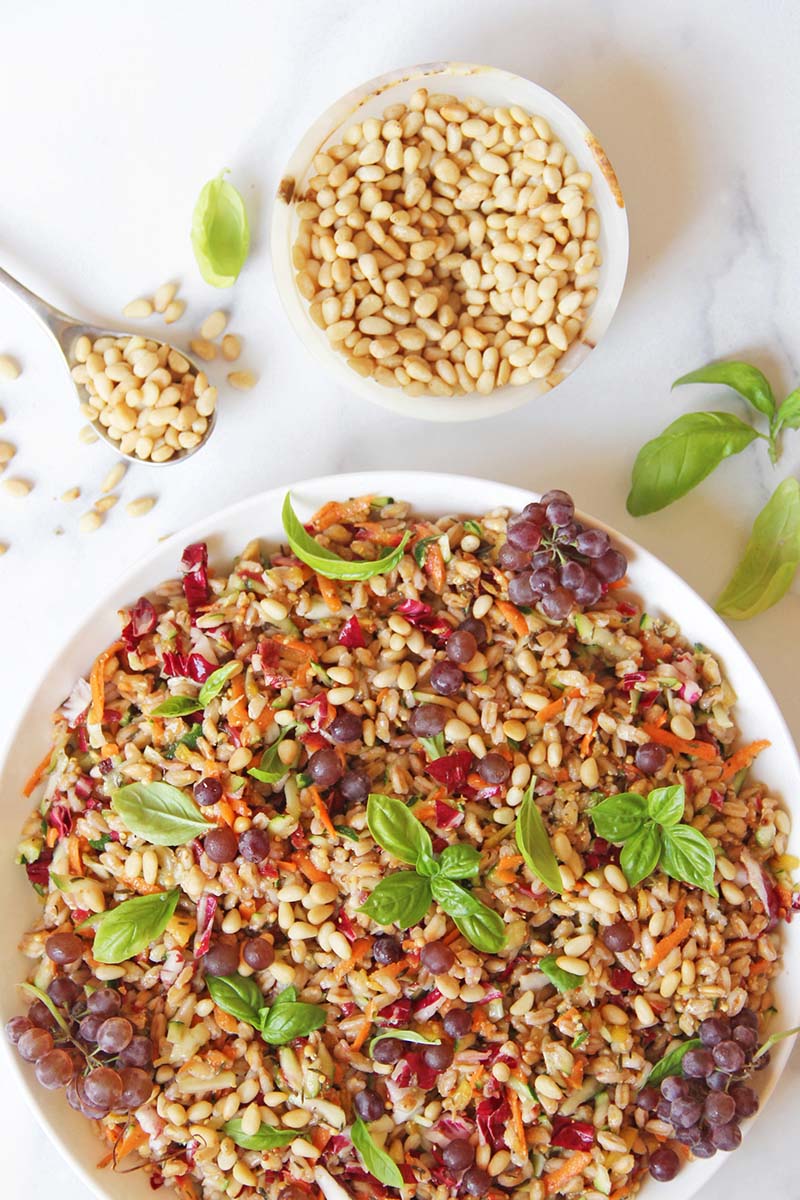 Mediterranean farro salad in a serving bowl, shown with pine nuts and fresh basil.