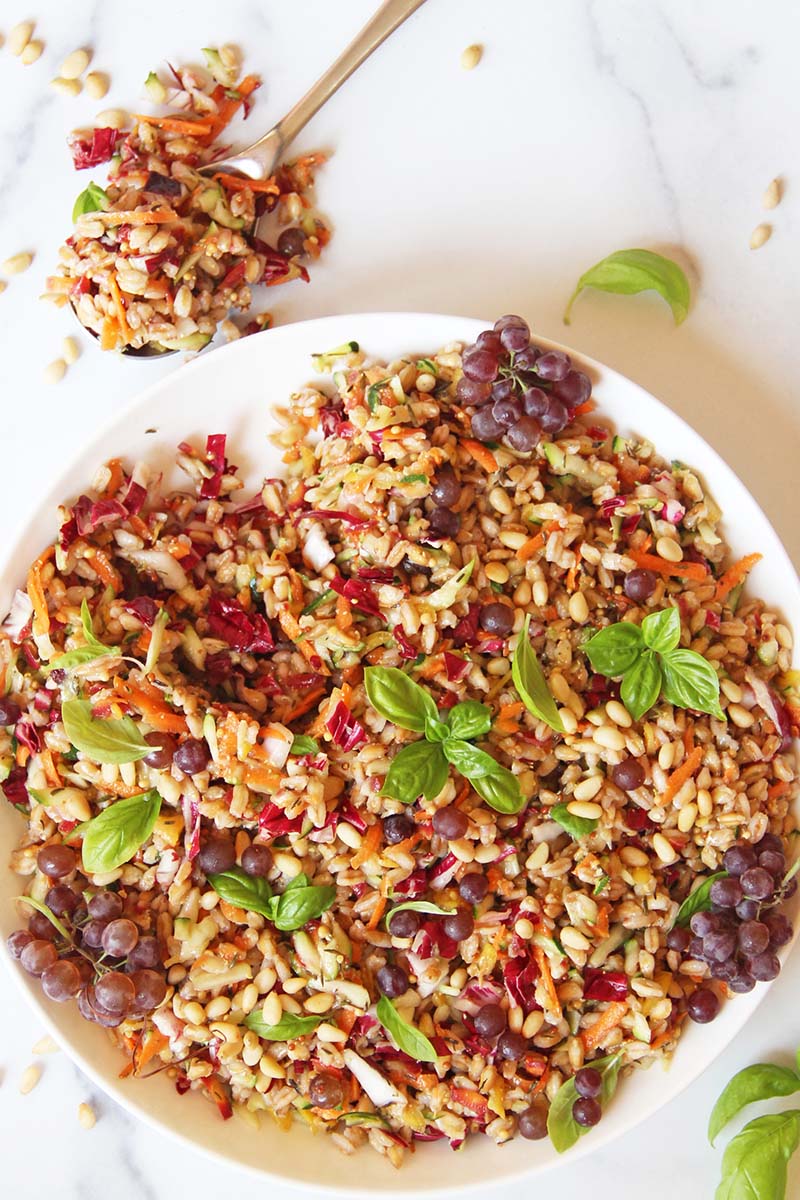 Serving bowl of a colorful summer farro salad with vegetables, shown on a white background.