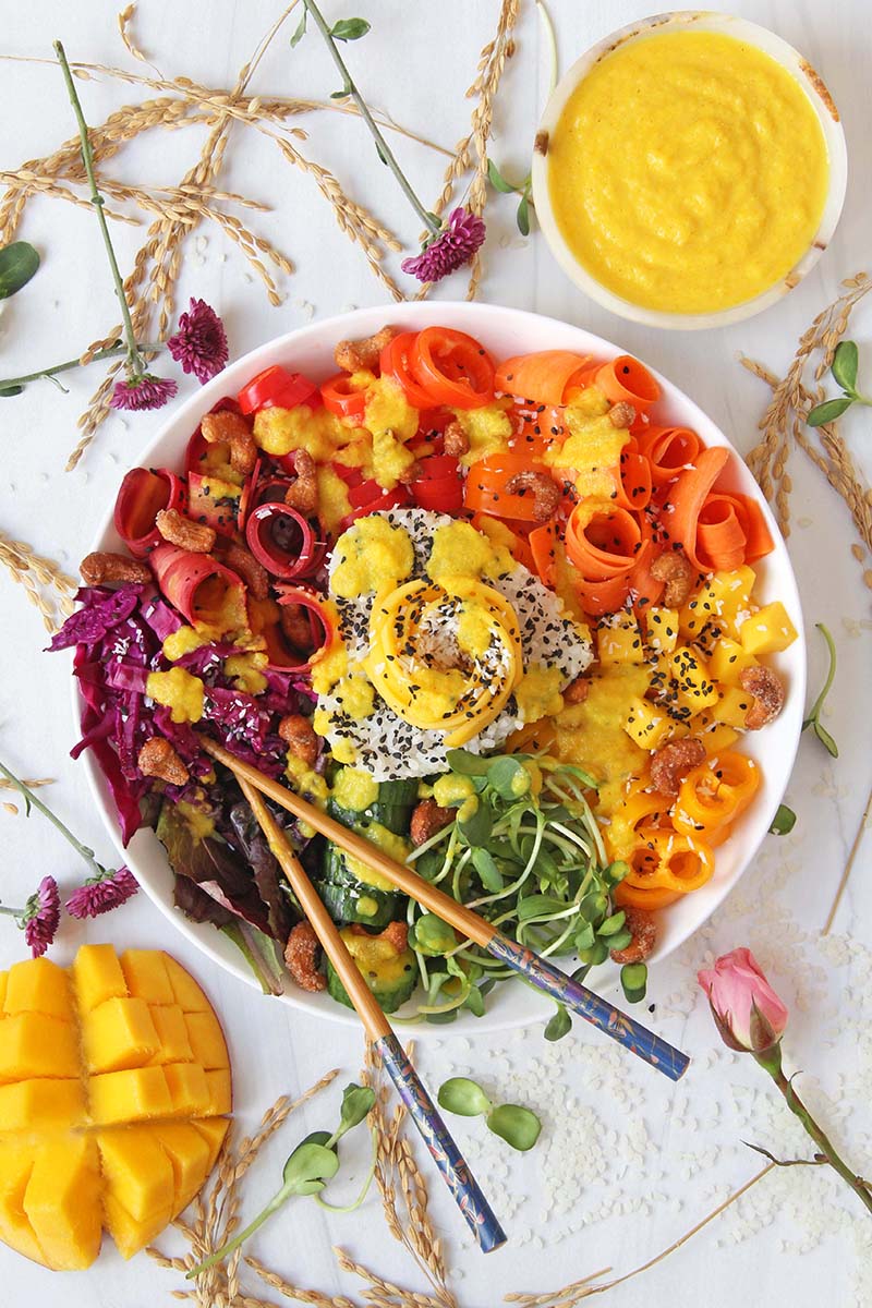 Overhead view of a vegan rice bowl meal, after a vibrant yellow spicy mango sauce has been drizzled on top.