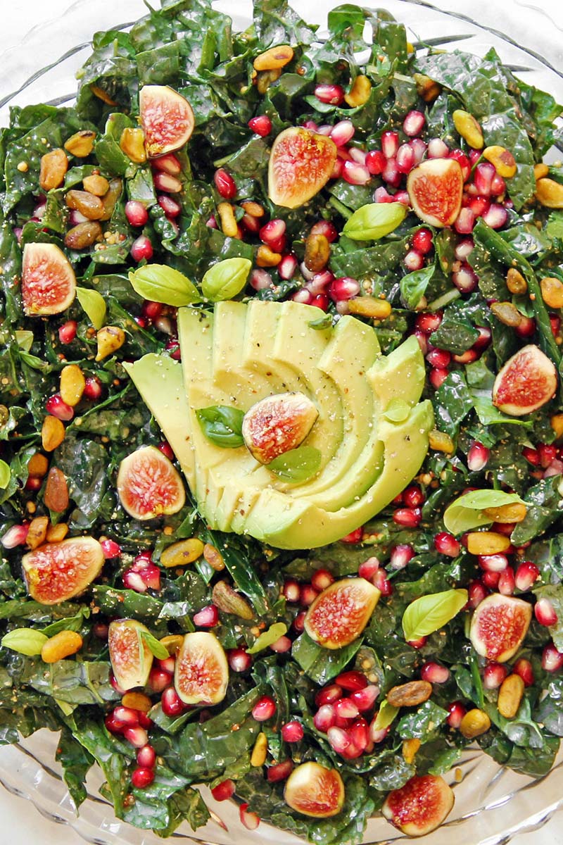 Close-up of a fall kale salad with fresh figs, avocado, pomegranate, pistachios, and basil.