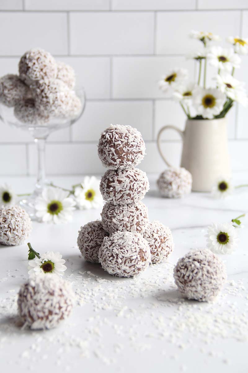 Stack of chickpea protein truffles, coated in shredded coconut and shown against a white kitchen tile background.