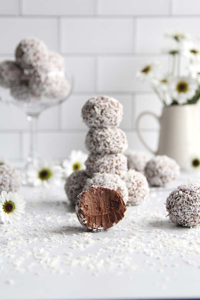 A single chocolate chickpea truffle in the foreground, with a stack of additional truffles in the background.