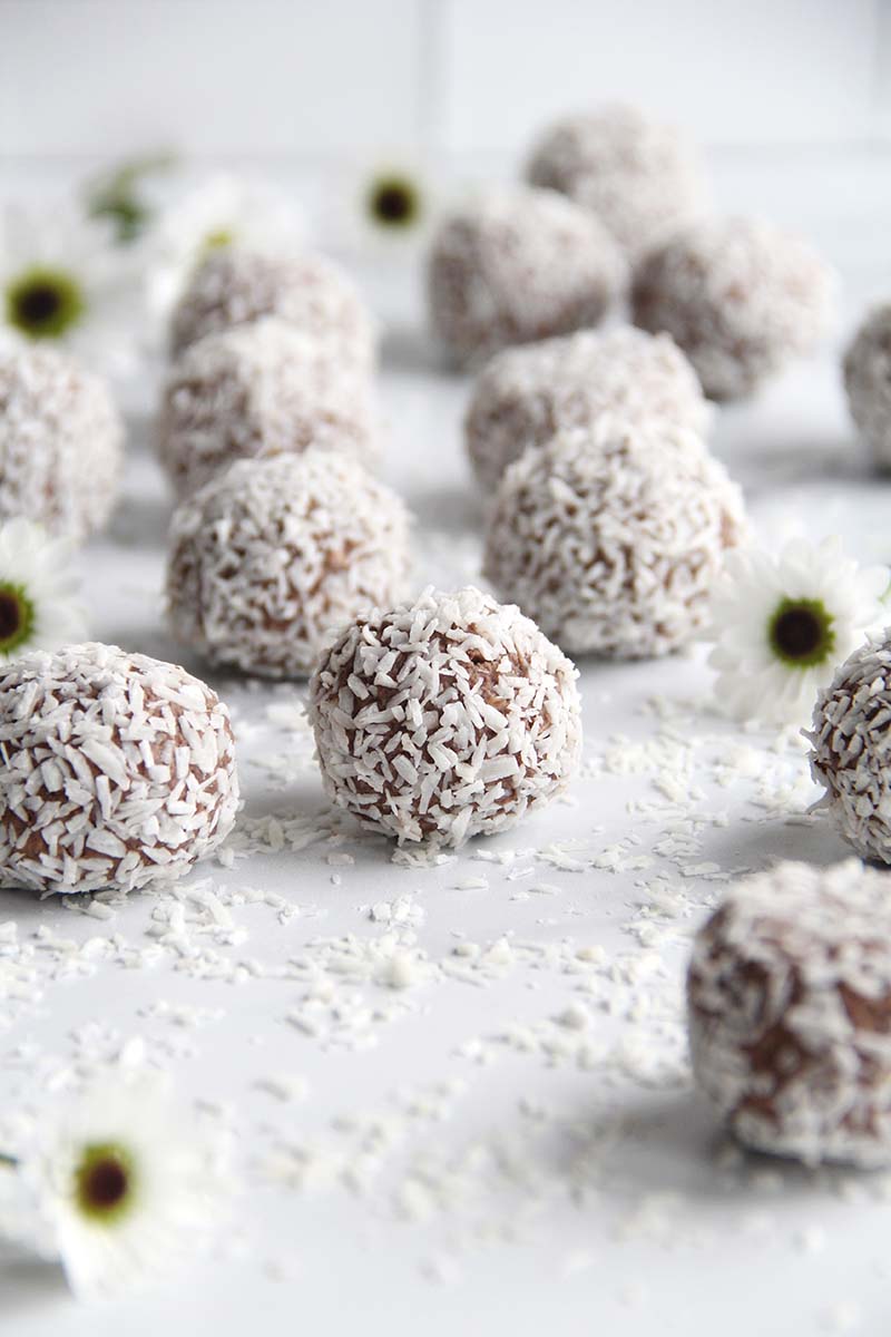 Close-up of chocolate chickpea truffles coated in shredded coconut, shown on a white surface.
