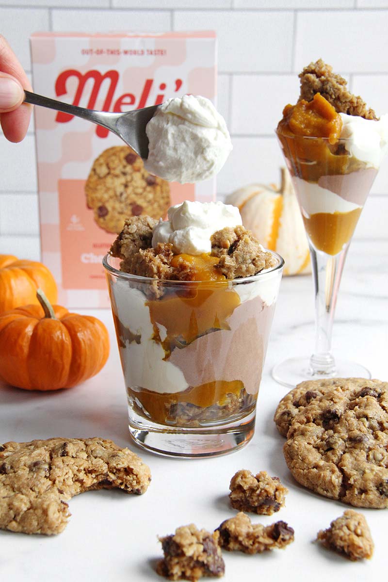 Woman's hand adding whipped cream on top of a trifle with cookies, chocolate yogurt, and pumpkin.