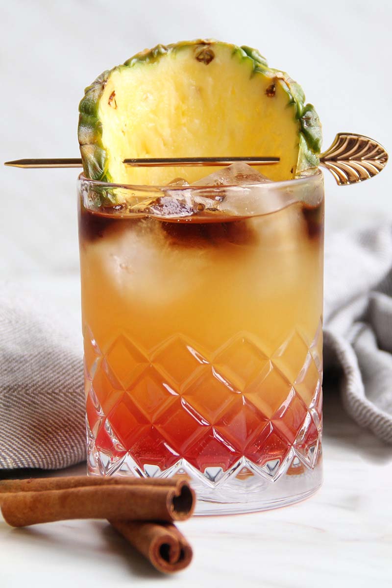 Close-up of a Chai Tai rum cocktail garnished with a pineapple slice on a white background.