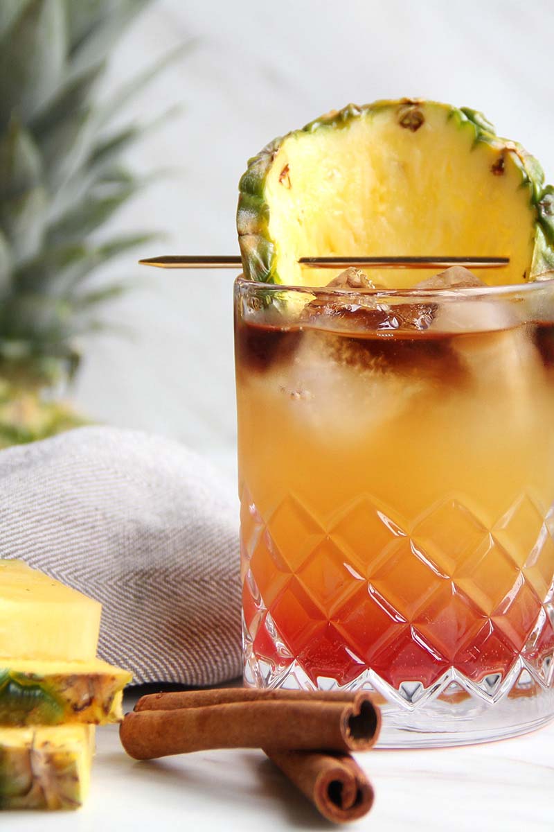 A fall Mai Tai variation, shown with cinnamon sticks and pineapple wedges.