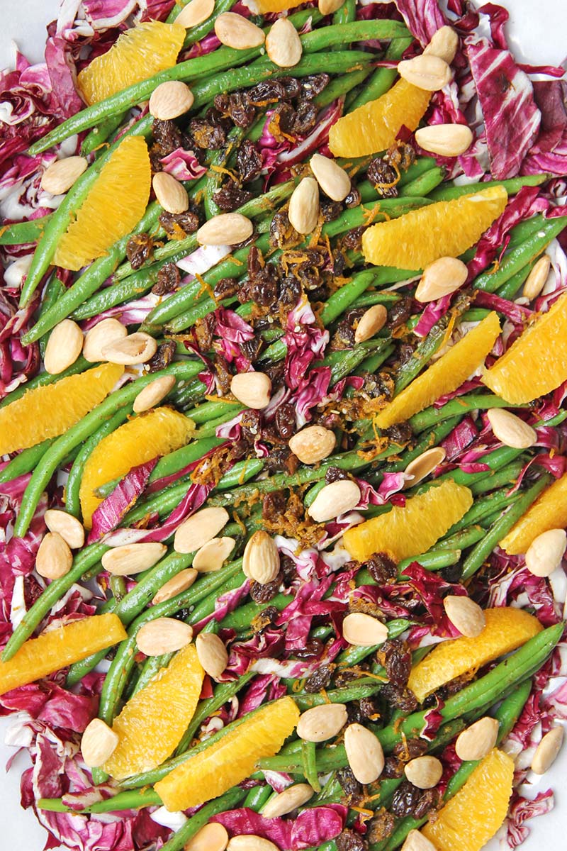Spanish green beans on a white platter, topped with orange segments and marcona almonds.