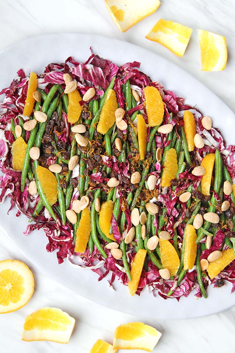 Overhead view of a platter of colorful green beans with orange and radicchio.