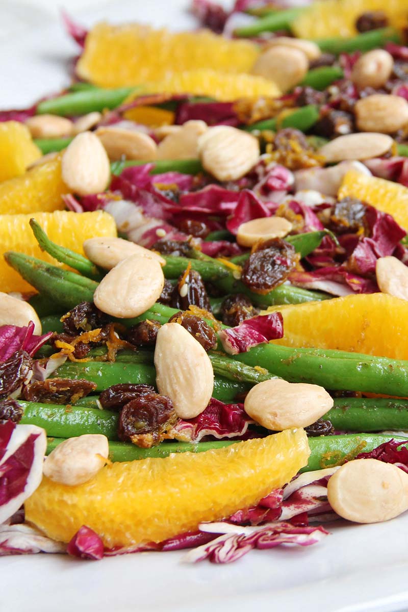 Close-up of Spanish green beans topped with orange, almonds, raisins, and radicchio.