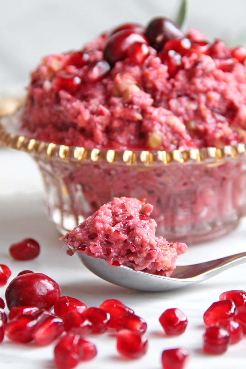 Close-up of a spoonful of vibrantly-colored pomegranate cranberry sauce, with the bowl of cranberry sauce in the background.