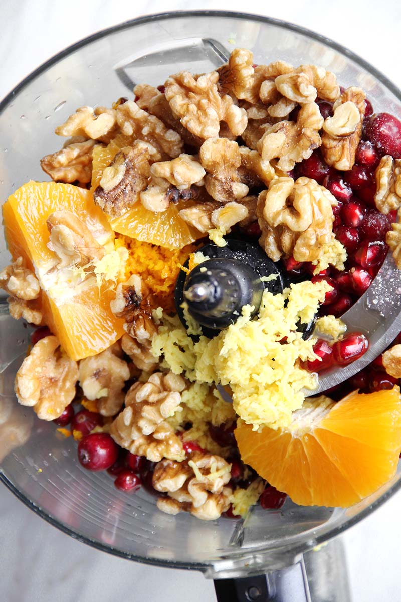 Ingredients for no-cook pomegranate cranberry sauce, shown from above in the bowl of a food processor.