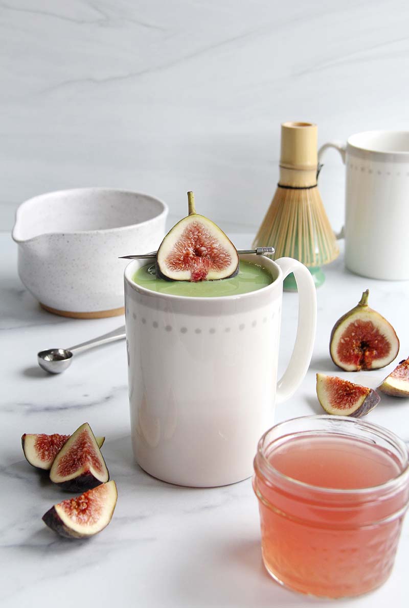 Fig matcha latte in a white kitchen, showing the contrast between the bright green matcha and the pink-red fig garnish.