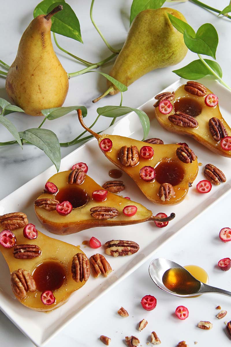 Rum poached pears on a white serving platter, shown next to whole pears.