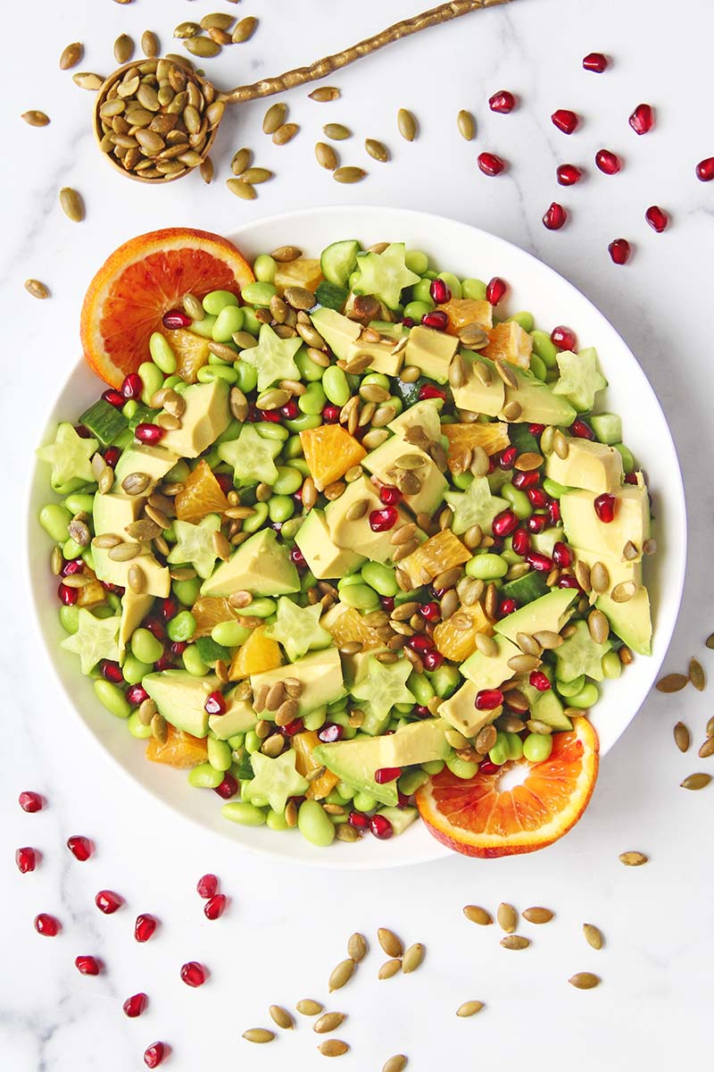 Overhead view of a healthy edamame salad for the holidays, topped with orange slices, pomegranate, and pepitas.