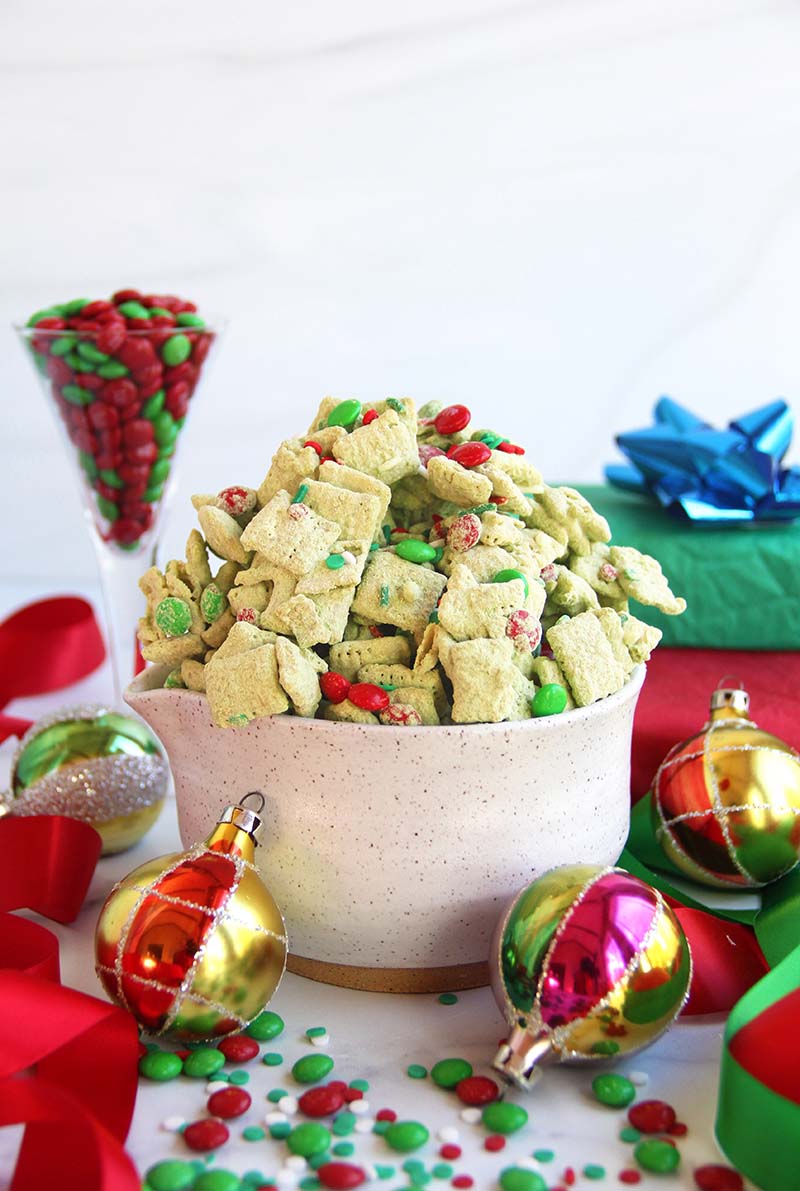 No-bake Christmas matcha puppy chow in a white bowl, featuring a bright green color and festive red and green sprinkles.