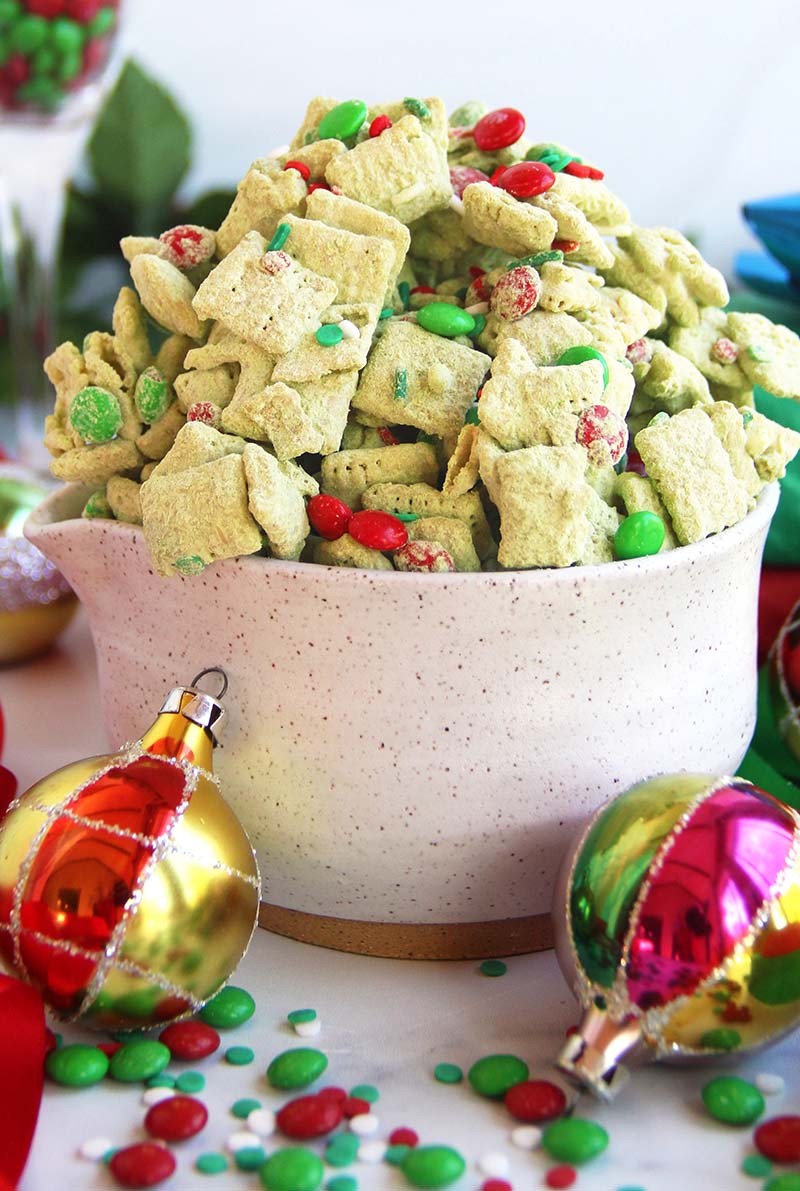 Close-up of Christmas matcha puppy chow coated in powdered sugar and matcha, with red and green sprinkles and chocolate candies.