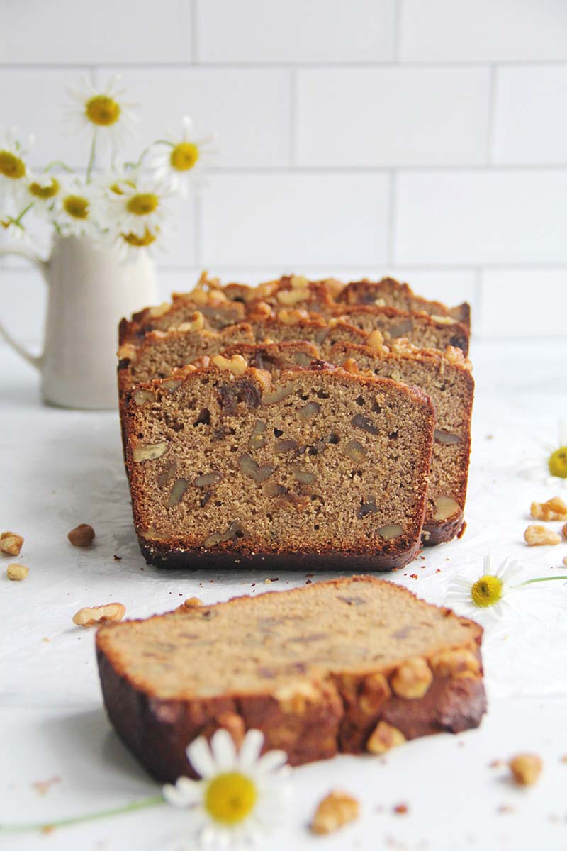 Slices of chickpea flour banana bread arranged on a marble countertop, with one thick slice turned on its side showing the dense, moist crumb and golden brown crust.