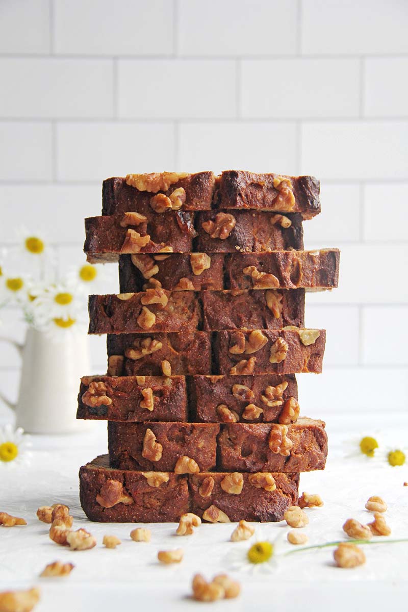Stacked slices of vegan chickpea flour banana bread topped with walnuts, photographed from the side to show the golden crust topped with extra walnuts.