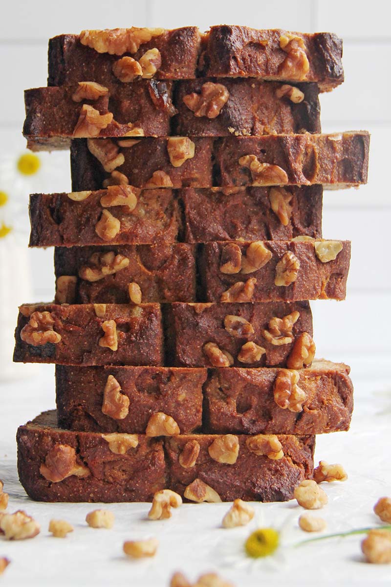 Stacked slices of vegan chickpea flour banana bread topped with walnuts, viewed from the side to emphasize the hearty, protein-rich texture.