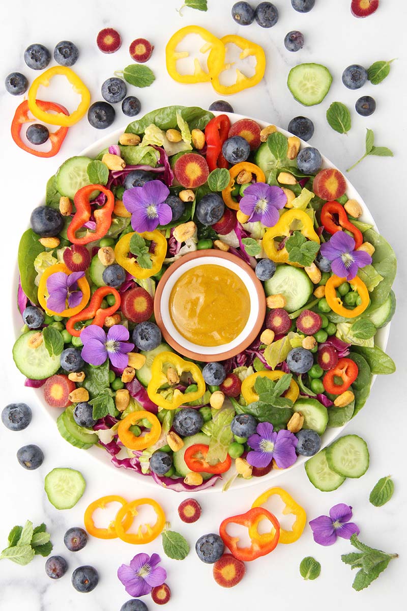 Turmeric tahini sauce used as a creamy salad dressing on a healthy, rainbow salad with raw veggies.