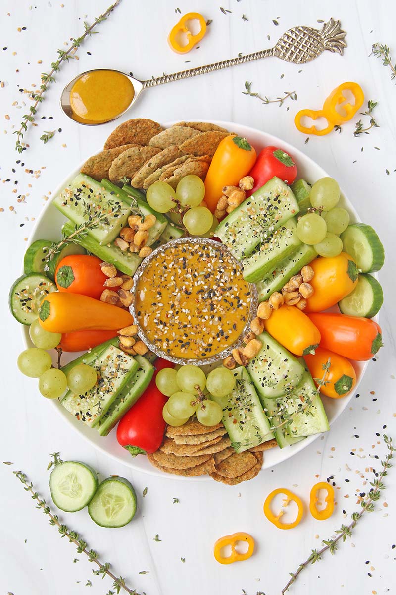 Thick and creamy turmeric tahini dip served with fresh vegetables, crackers, and grapes.