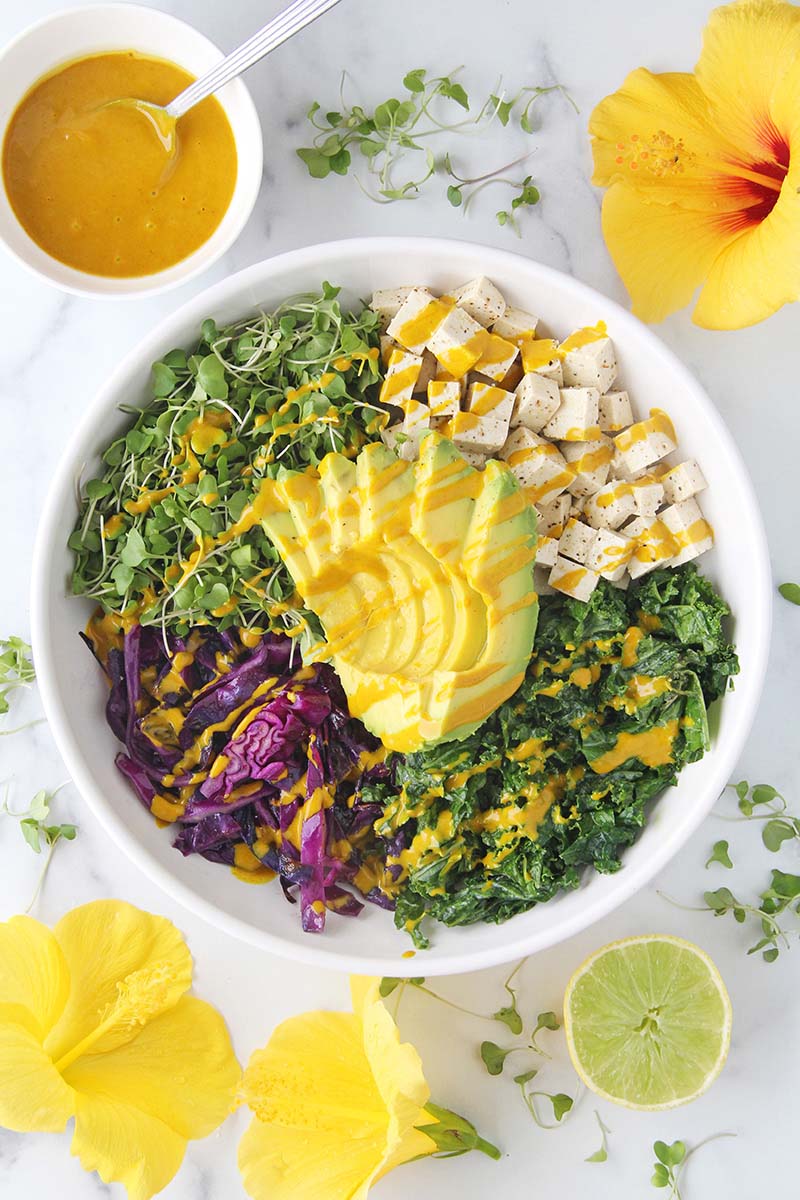 Turmeric tahini sauce drizzled over a nourishing bowl meal with greens, tofu, and avocado.