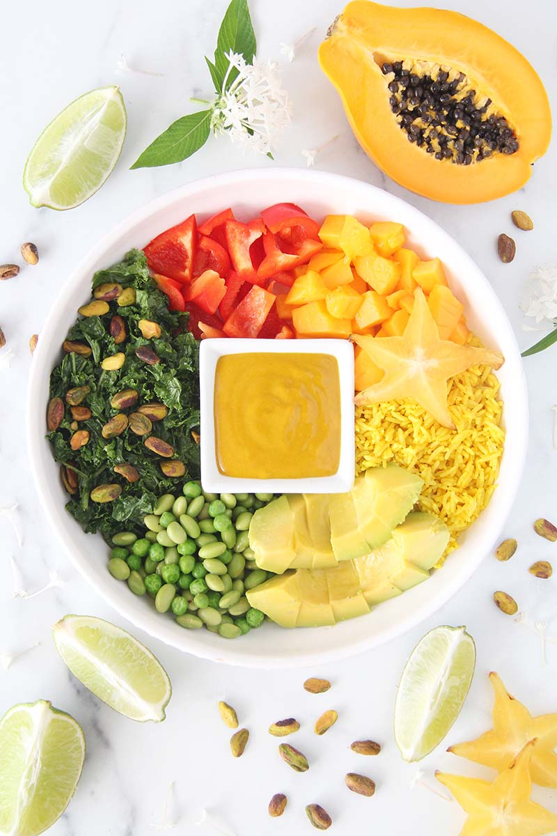 Turmeric tahini sauce showed in a small square dish at the center of a healthy and vegan rainbow bowl meal.