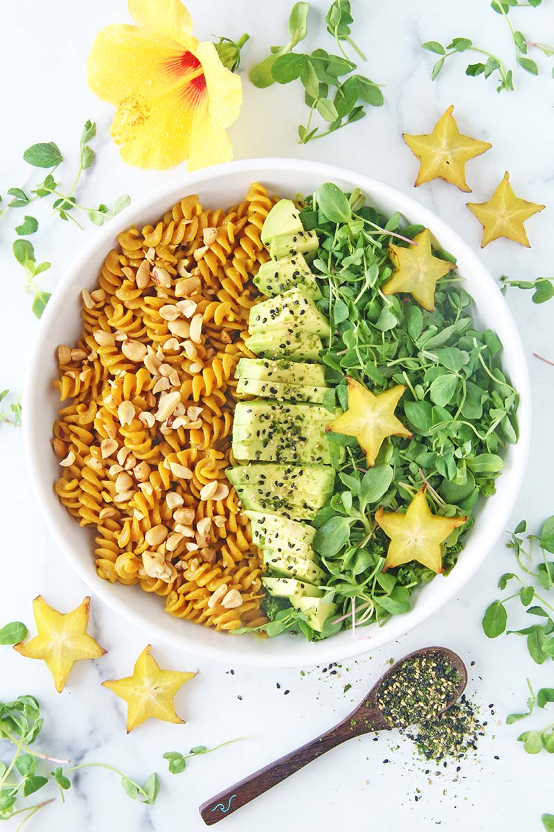Individual serving of creamy golden turmeric pasta in a white bowl, served with a green salad and sliced avocado.