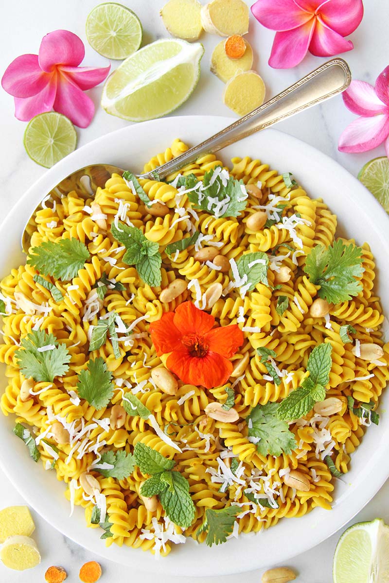 Colorful vegan turmeric pasta in a serving dish, garnished with peanuts, fresh herbs, and coconut.