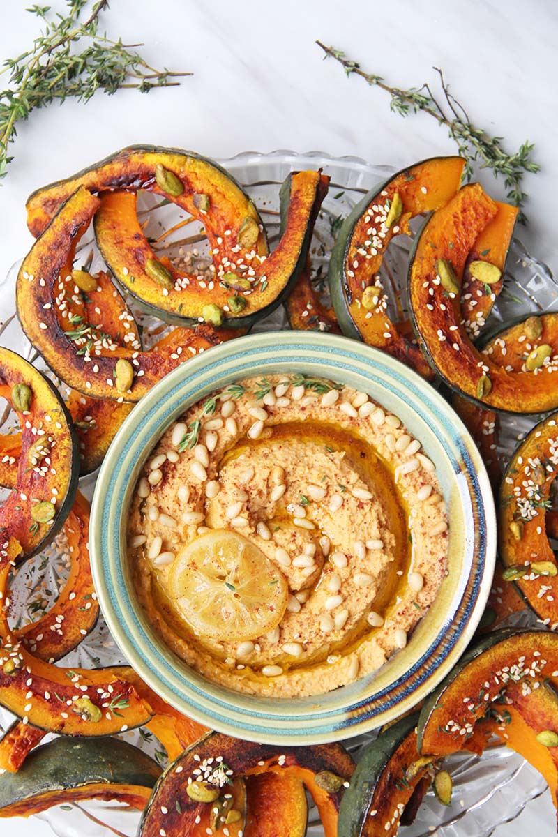 Sumac-roasted kabocha squash dippers garnished with pistachios and sesame seeds, served as a hearty vegan appetizer with lemon hummus.