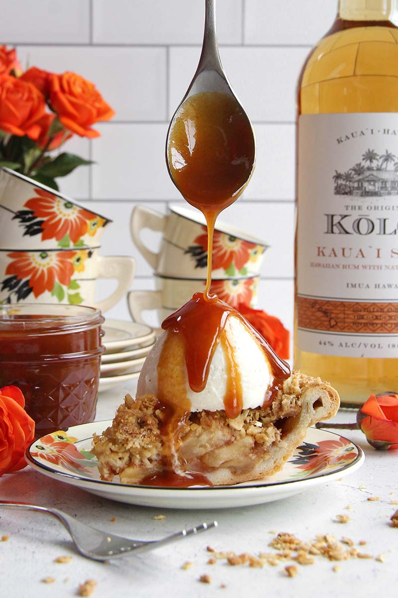 Close-up of rum caramel sauce being spooned over ice cream and apple pie, with caramel cascading down the sides.