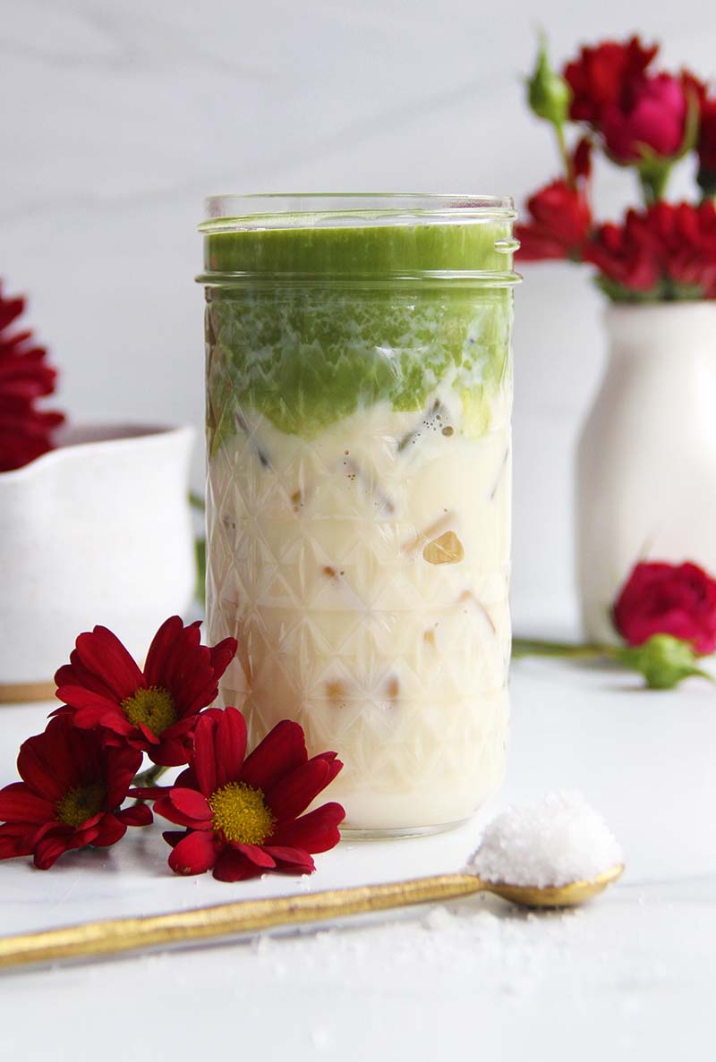 Close-up of an iced salted maple matcha latte in a glass jar, showing the creamy texture of the salted maple soy milk and the vibrant green matcha layer on top.