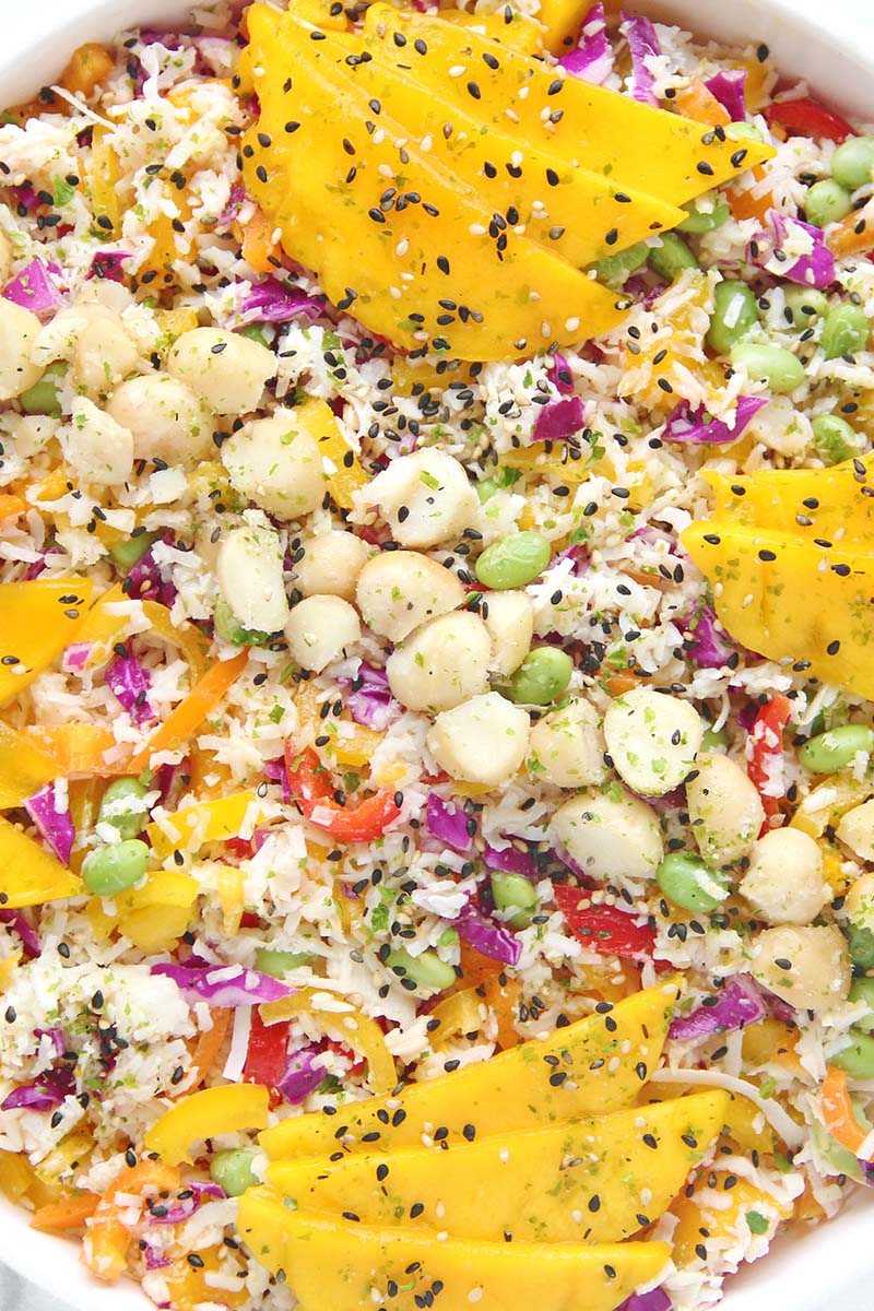 Close-up of a no-cook tropical hearts of palm rice salad with mango, crisp colorful vegetables, macadamia nuts, and furikake seasoning.