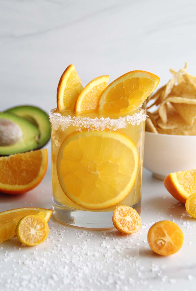 Spiced orange margarita made with both tequila and spiced rum, served with a salted rim and fresh orange slices, styled with tortilla chips and avocado for a winter party.